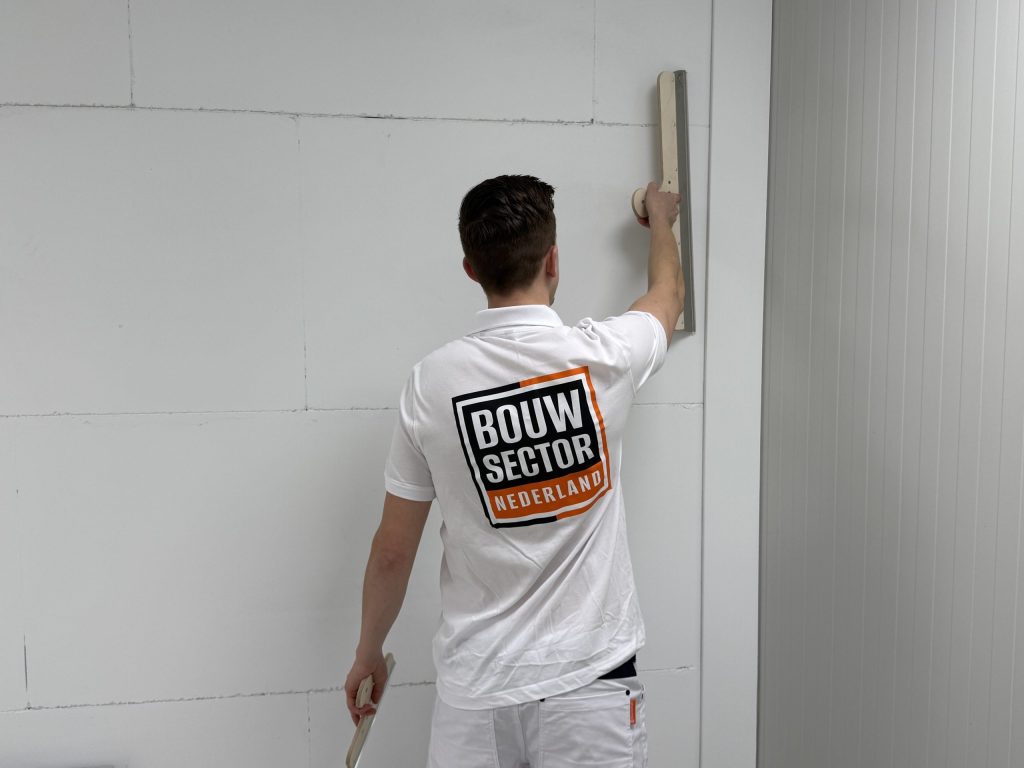 Stukadoor in wit werktenue met het logo van Bouwsector Nederland trekt een wand glad met een stucspaan