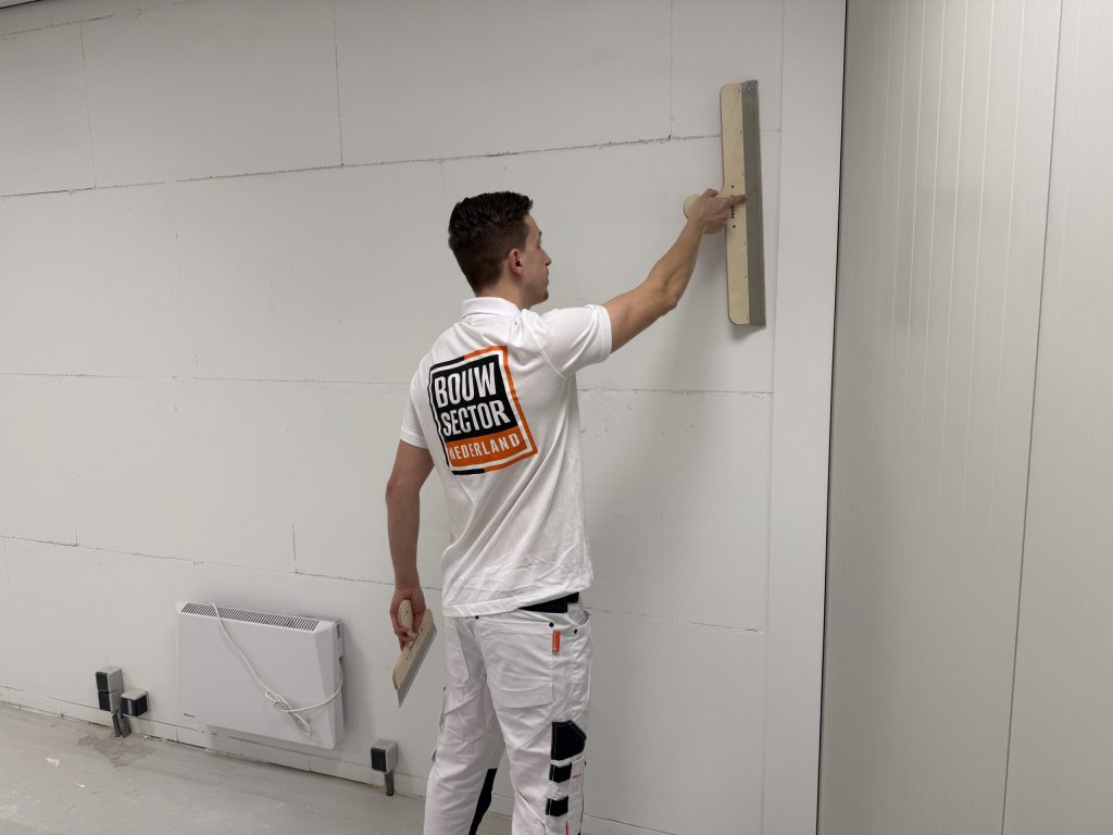 Stukadoor trekt met een lange spaan een wand van gipsblokken vlak in een lege ruimte